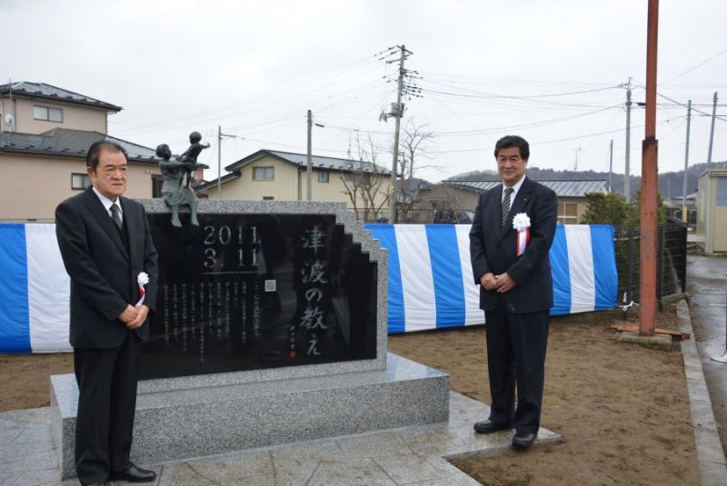 石碑の前に立つ牛網町内会の佐藤充信会長（左）と東北ミサワホームの佐藤春夫社長